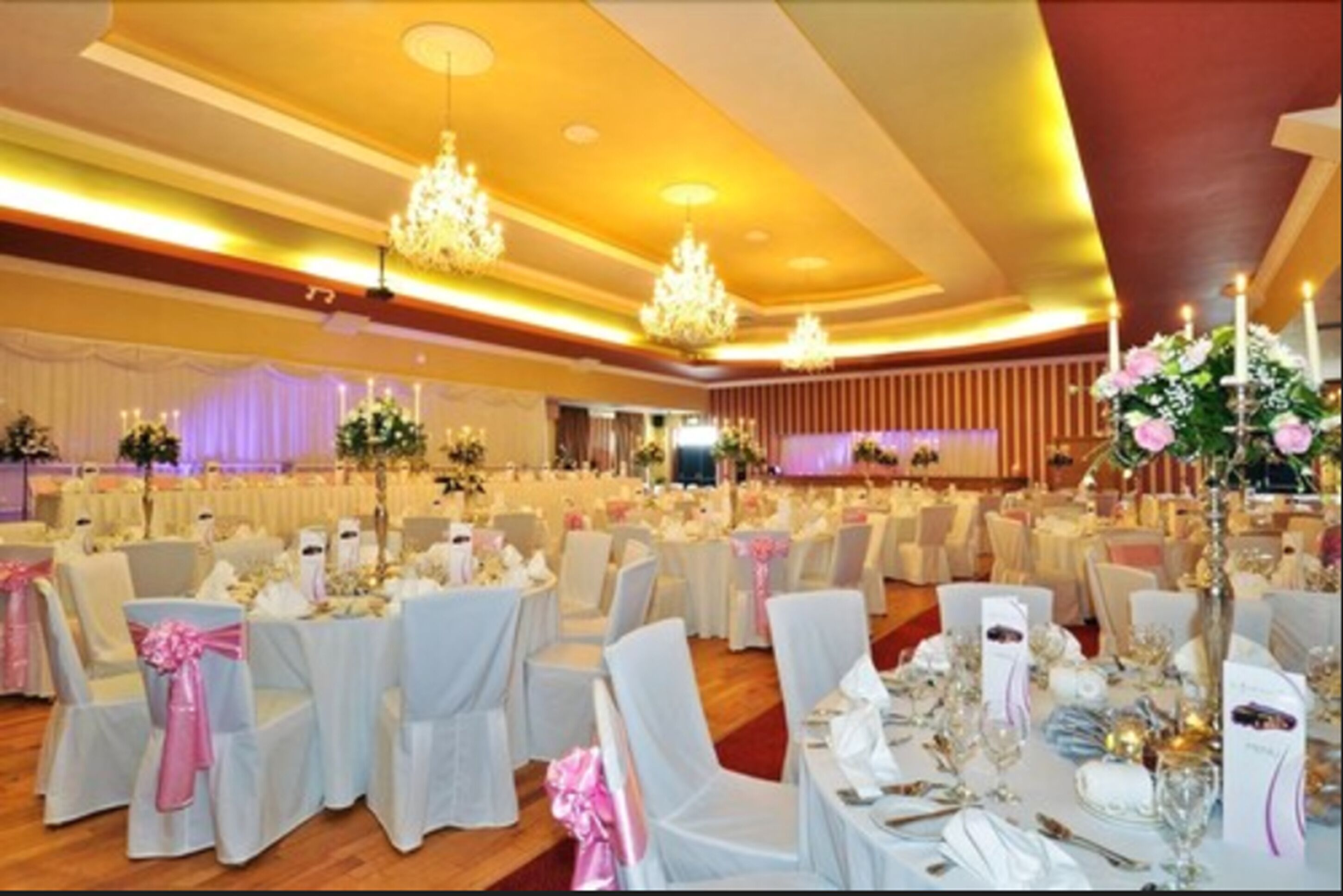 A banquet hall with round tables, white tablecloths, and chairs with pink sashes.