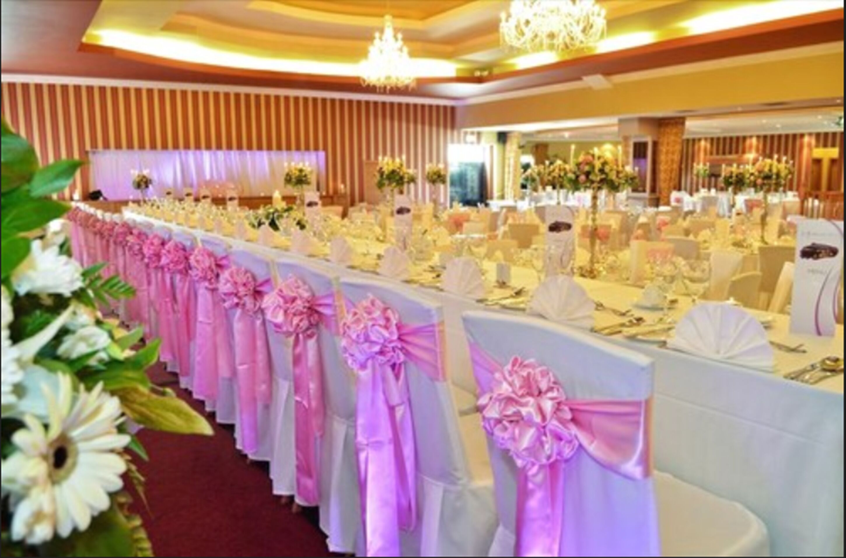 A banquet hall with rows of tables, each with white tablecloths and pink sashes.