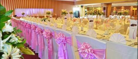 Un salón de banquetes con filas de mesas, cada una con manteles blancos y cintas rosas.