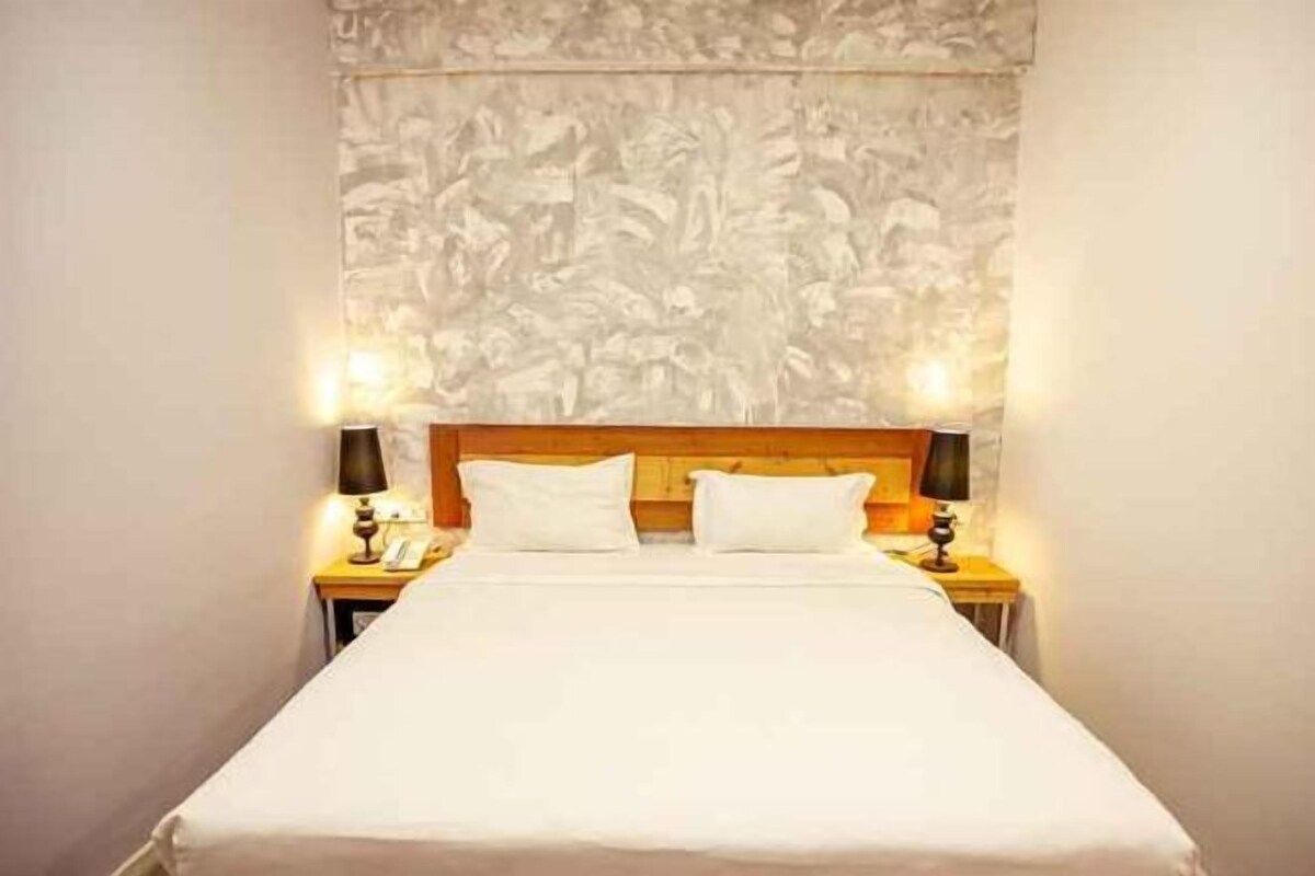 Een hotelkamer met een groot bed, twee bedlampjes en een gestructureerde wand achter het bed.