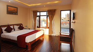 A hotel room with a large bed, a chair, a TV, and a view of the city through the window. - Thamel Grand Hotel (Kathmandu)