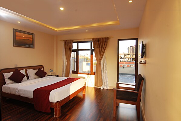 A hotel room with a large bed, a chair, a TV, and a view of the city through the window. - Thamel Grand Hotel (Kathmandu)