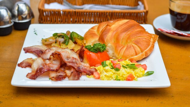 A breakfast plate with bacon, eggs, tomatoes, and a croissant on a white plate. - Thamel Grand Hotel (Kathmandu)