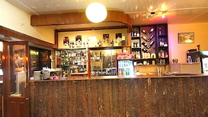 A bar area with a wooden counter, shelves with bottles, a Coca-Cola sign, and a refrigerator. - Thamel Grand Hotel (Kathmandu)