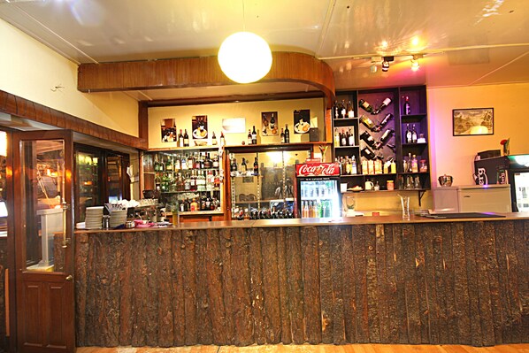 A bar area with a wooden counter, shelves with bottles, a Coca-Cola sign, and a refrigerator. - Thamel Grand Hotel (Kathmandu)