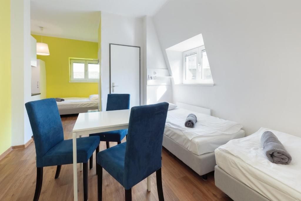 A compact room with a dining table and chairs, a bed with a rolled towel, and a window.