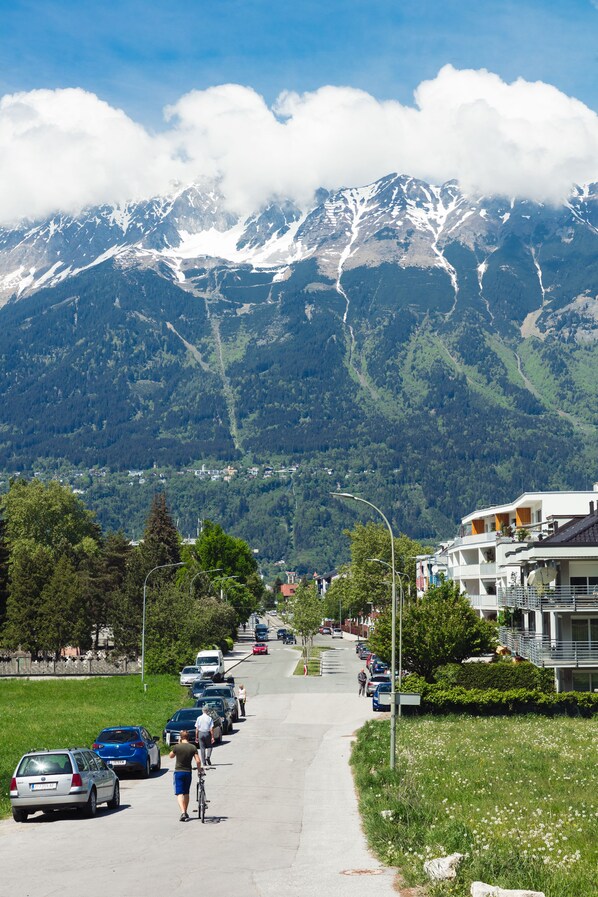 A road with parked cars and a cyclist, leading to a building with balconies overlooking a mountainous landscape. - Marmota Hostel (Innsbruck)