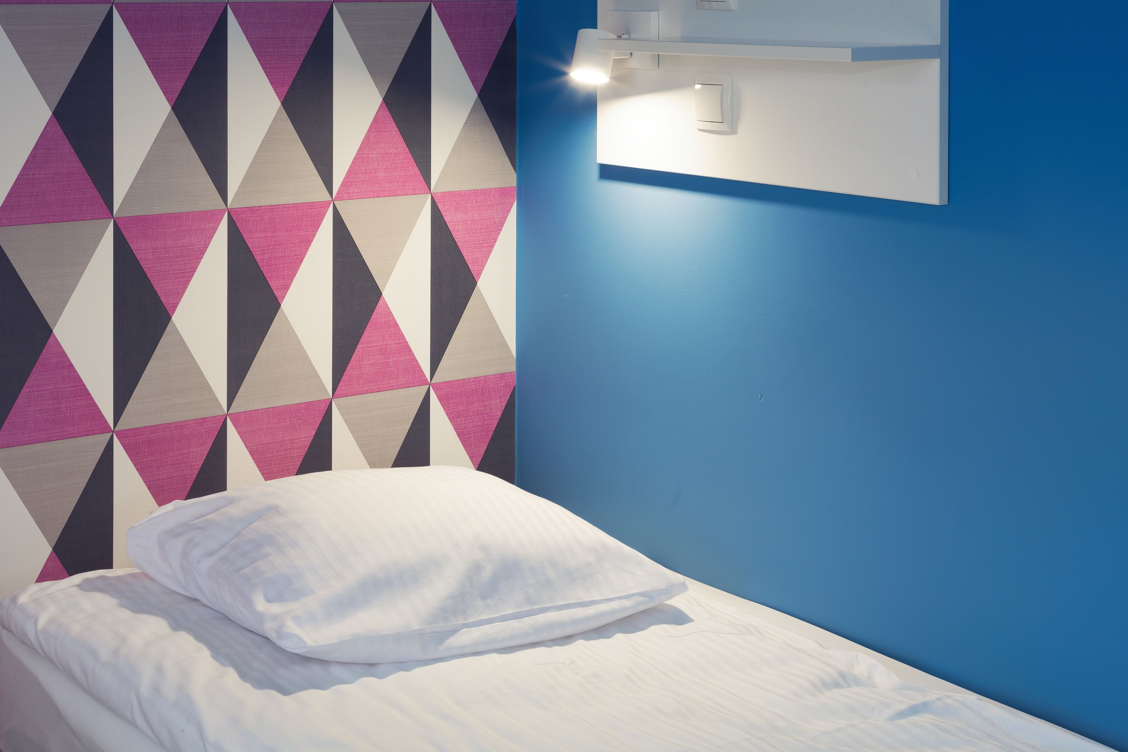 Una cama individual con ropa blanca en una habitación con pared de estampado geométrico y pared de acento azul.