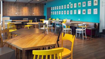 Un comedor moderno con mesas y sillas de madera, una pared de acento color aguamarina y obras de arte.