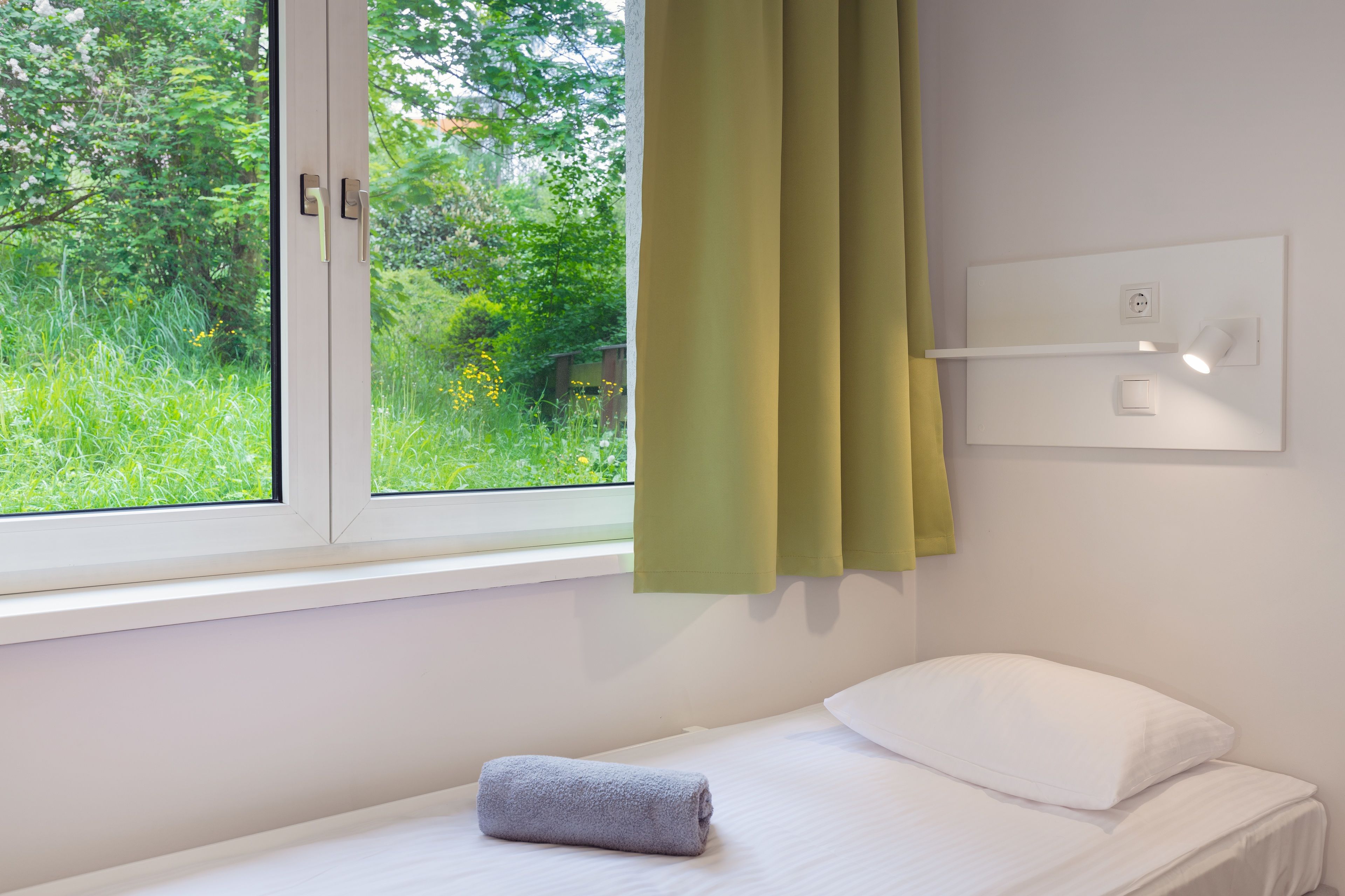 Una habitación de hotel con una cama individual, una ventana con cortinas y un interruptor de luz en la pared.