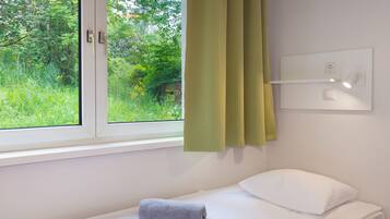 Una habitación de hotel con una cama individual, una ventana con cortinas y un interruptor de luz en la pared.
