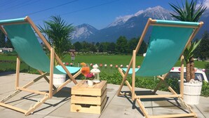 Two wooden beach chairs with green fabric, a wooden crate, and a small table with a lantern and flowers. - Marmota Hostel (Innsbruck)