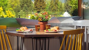 A dining table with chairs, a plate of food, a drink, and a flower arrangement. A mountain view is visible through a window. - Marmota Hostel (Innsbruck)