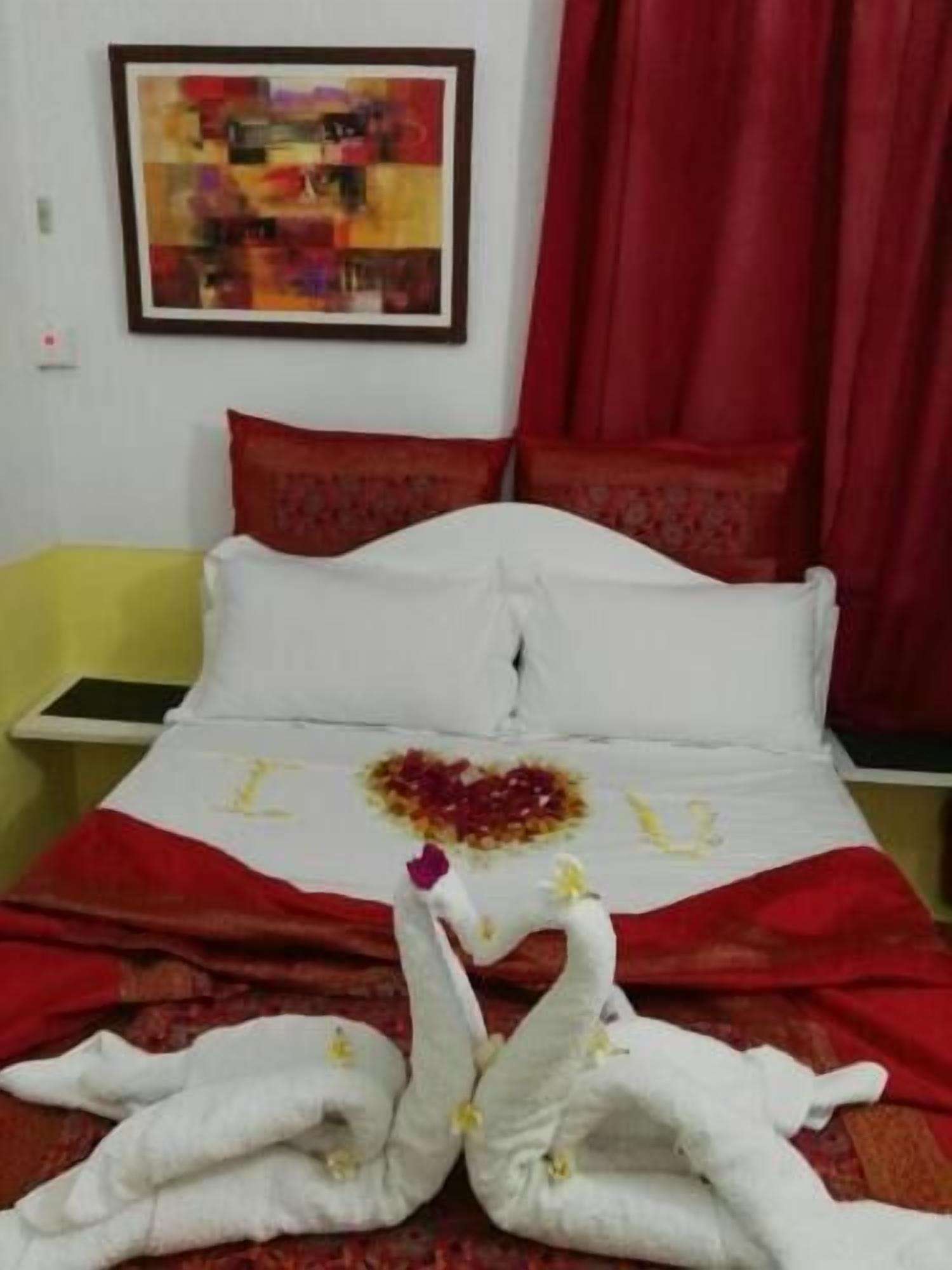 Uma cama com colcha vermelha e branca, uma decoração em formato de coração na cama e um quadro na parede.