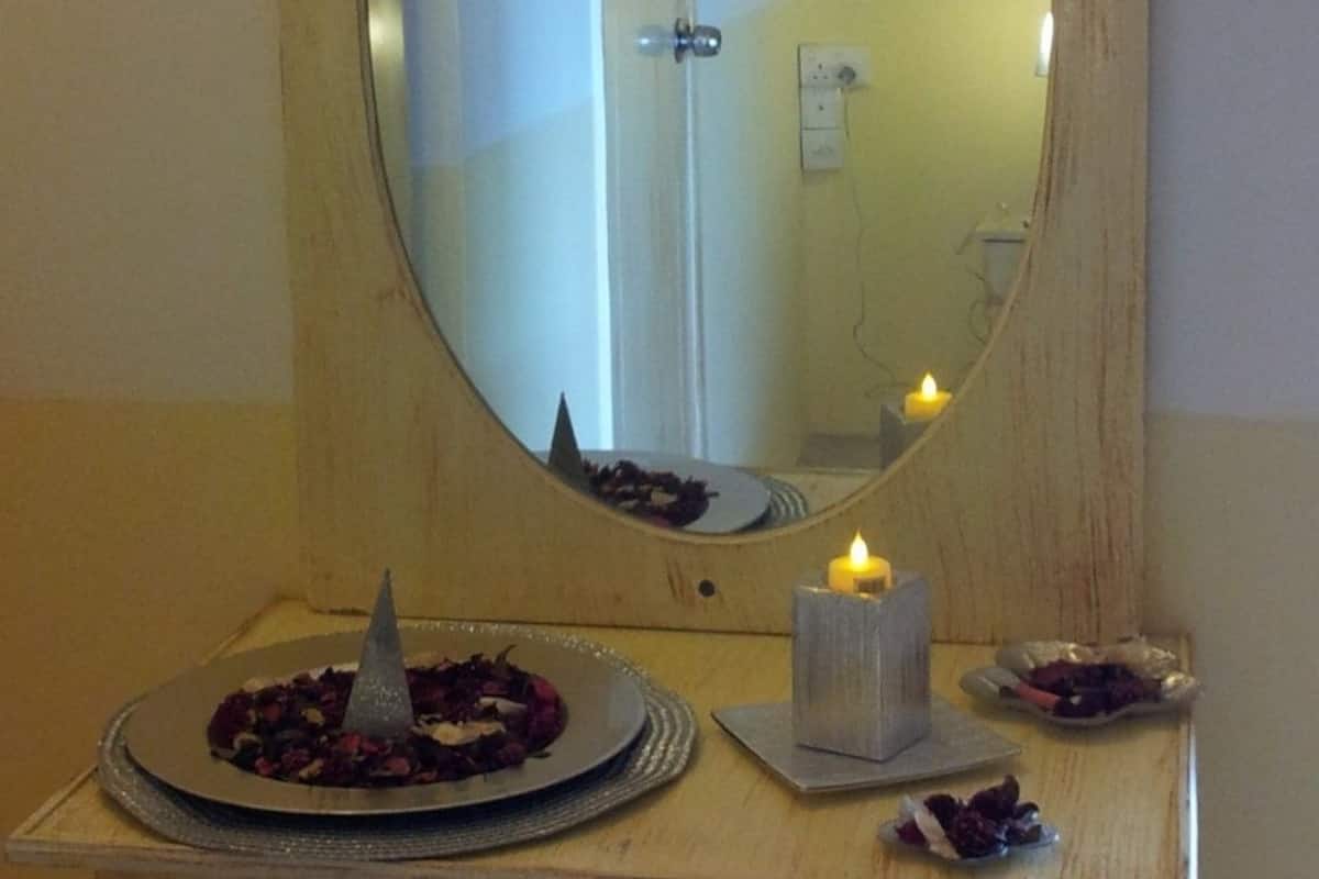 A mirror with a wooden frame, a candle, and a plate with dried flowers on a wooden dresser.