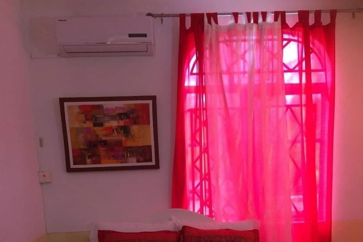 A hotel room with a bed, a painting on the wall, and a window with red curtains.