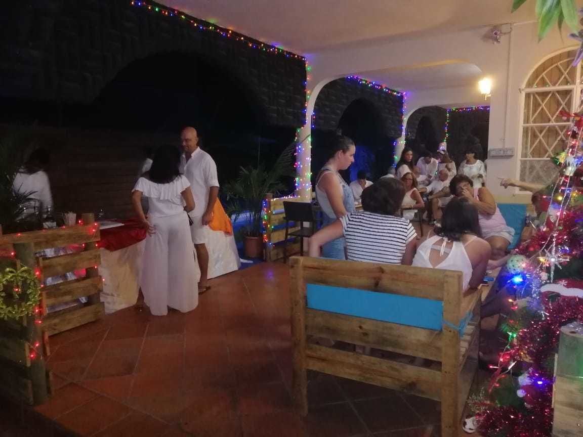 Un comedor interior con bancos y mesas de madera, decorado con luces de colores y un pequeño árbol de Navidad.