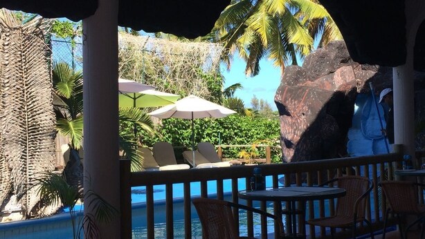 Ein Poolbereich mit Liegestühlen und Sonnenschirmen, umgeben von tropischer Vegetation und einer großen Felsformation.