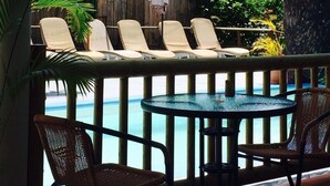 Ein Poolbereich mit Liegestühlen und einem Tisch, umgeben von Palmen und einem Holzzaun.