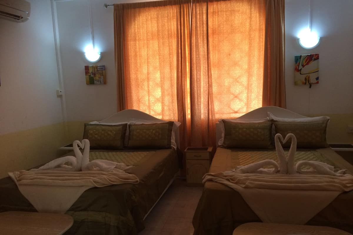 A hotel room with two beds, each with a towel swan decoration, a small table, and a wall-mounted light fixture.