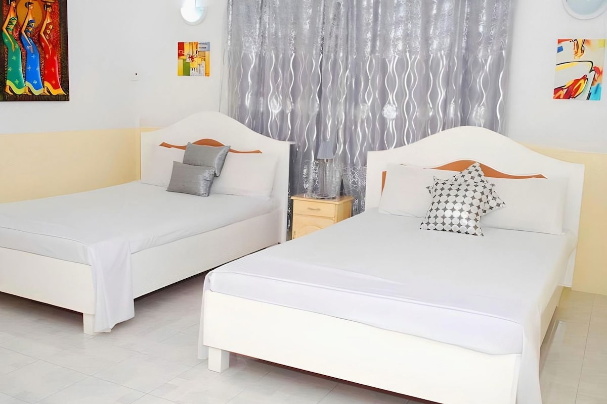 Two single beds with white bedding and wooden headboards, a small bedside table, and a decorative curtain.