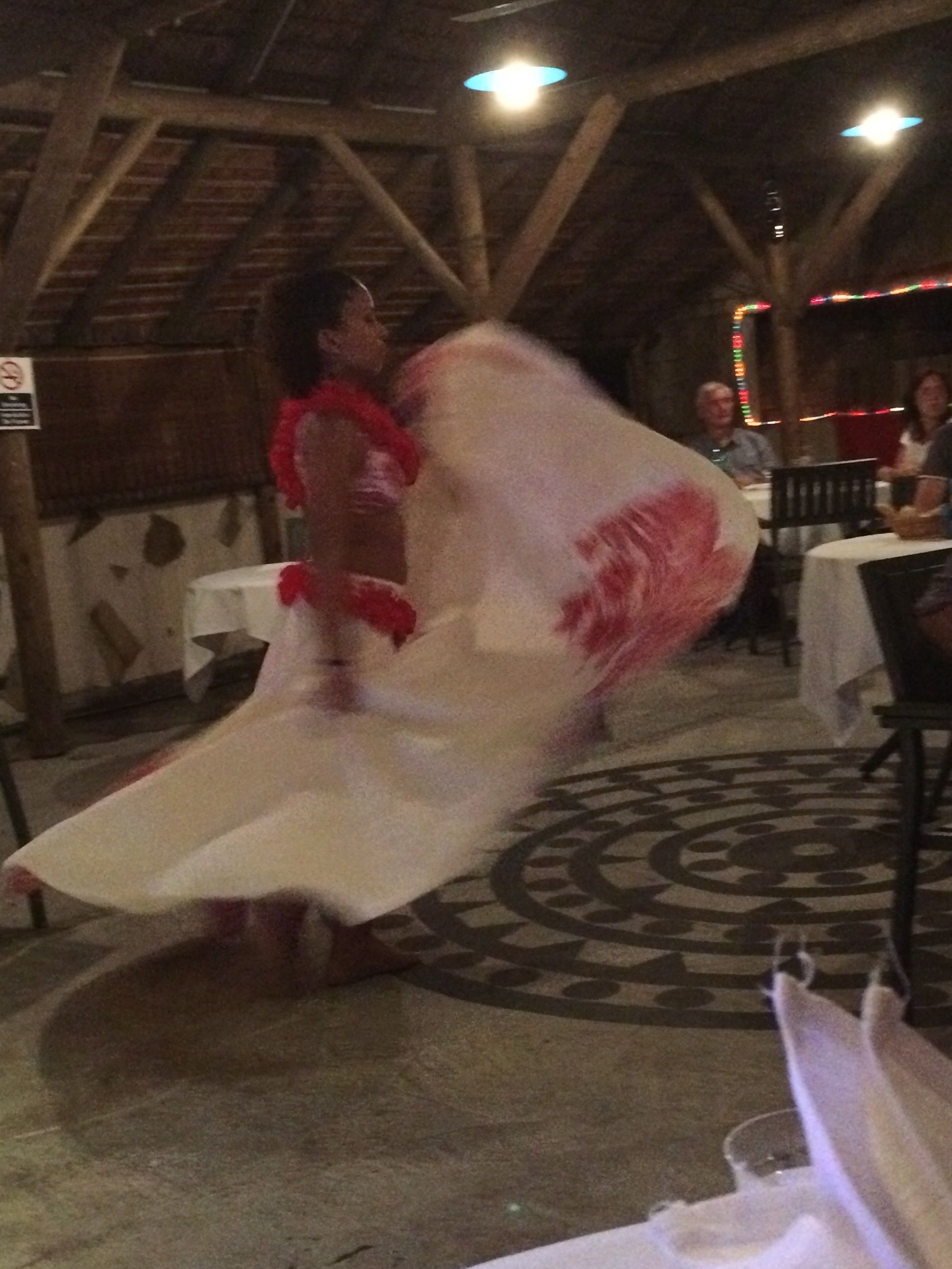 A person in a white dress with red accents, possibly performing or dancing, in an indoor setting with tables and chairs.