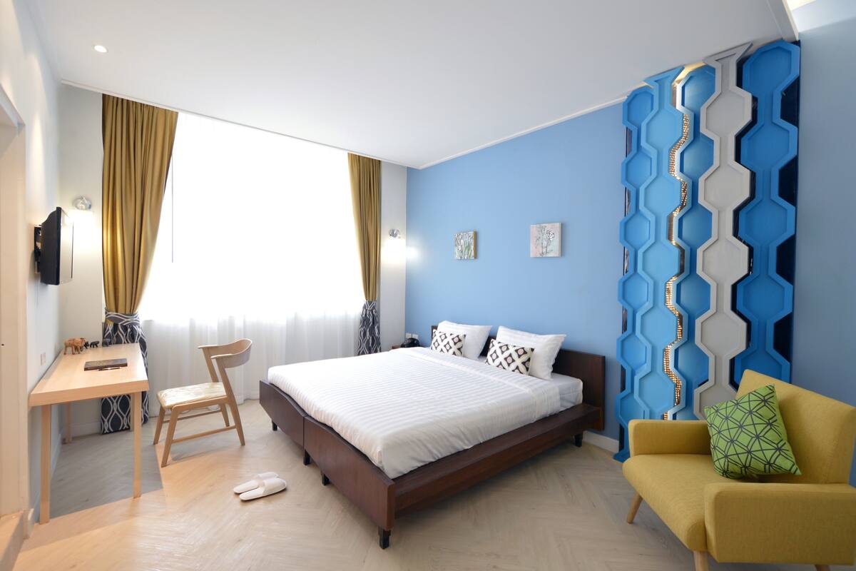A bedroom with a bed, a desk, a chair, a sofa, and a wall with a geometric pattern.