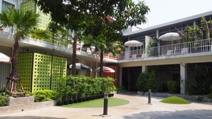 Un patio con una palmera, macetas verdes y una sombrilla blanca.