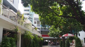 Un patio con una zona de estar cubierta, plantas en macetas y un edificio moderno al fondo.