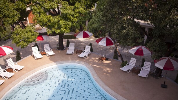 Una piscina con sillas de descanso y sombrillas, rodeada de árboles.