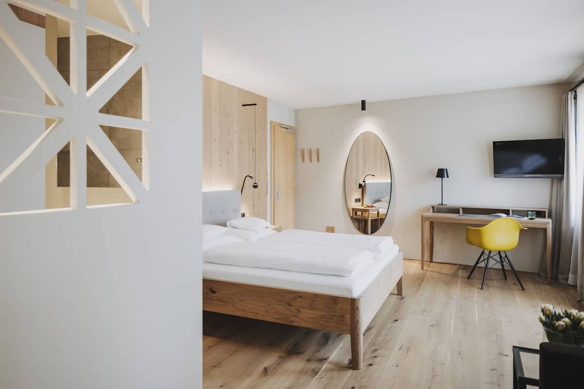 A modern bedroom with a wooden bed, a desk, a chair, and a TV.