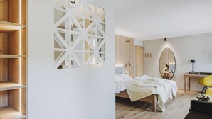 Un dormitorio moderno con suelo de madera, una cama con ropa de cama blanca, un escritorio con lámpara y una silla amarilla.