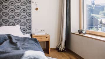 A bedroom with a patterned headboard, a bedside table with a lamp, a window with curtains, and a view of the outside.