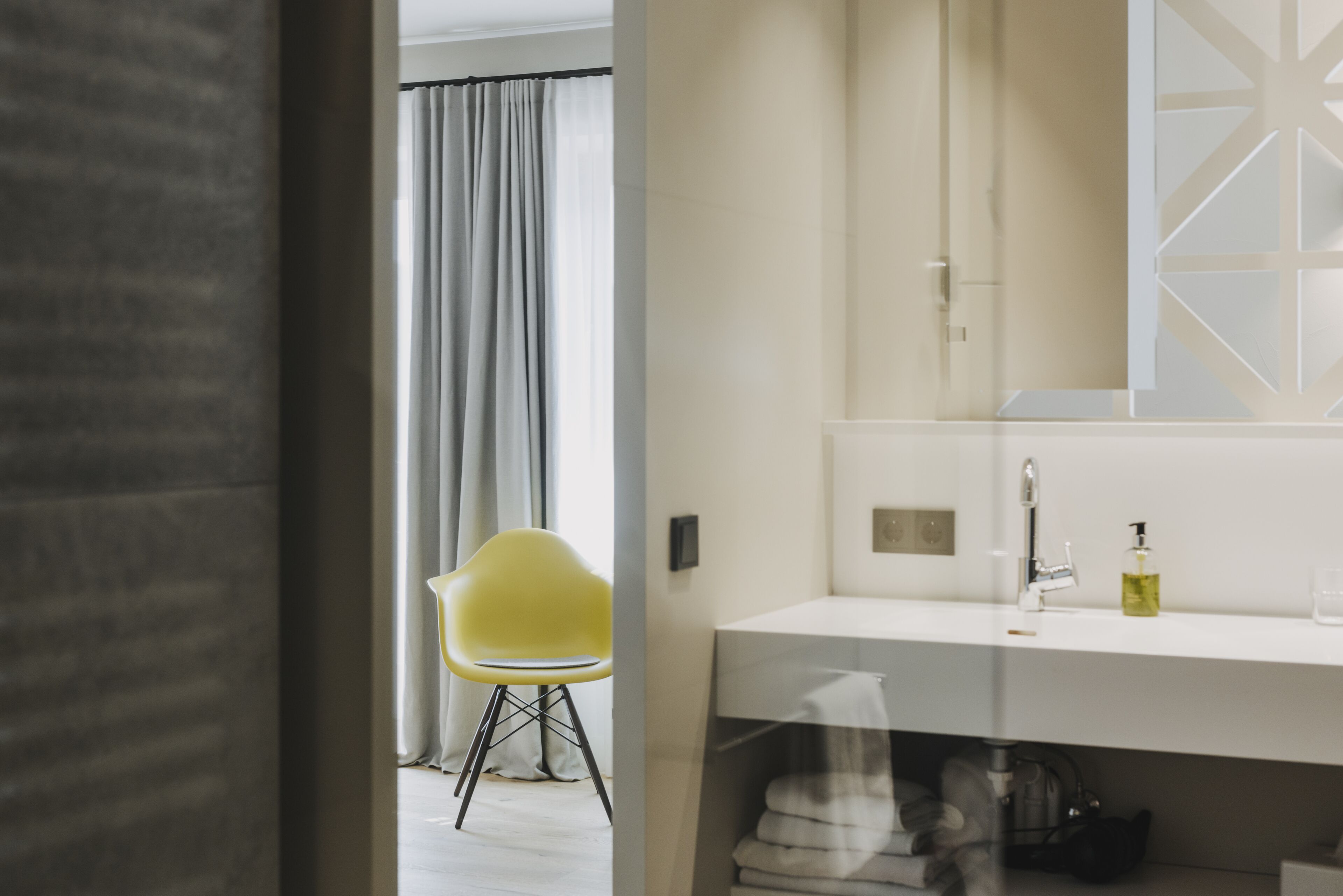 A modern bathroom with a white vanity, a yellow chair, and a large mirror.
