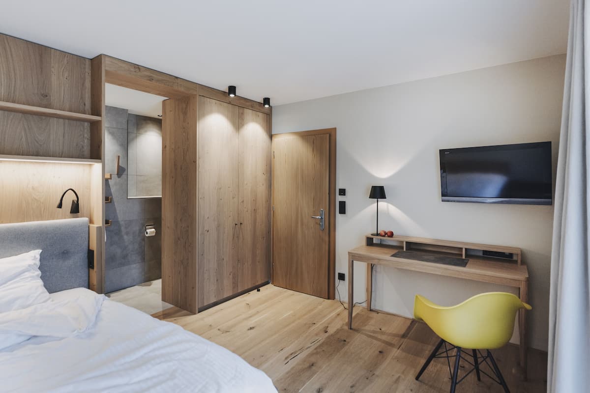 A modern hotel room with a bed, wooden wardrobe, desk, and a TV.