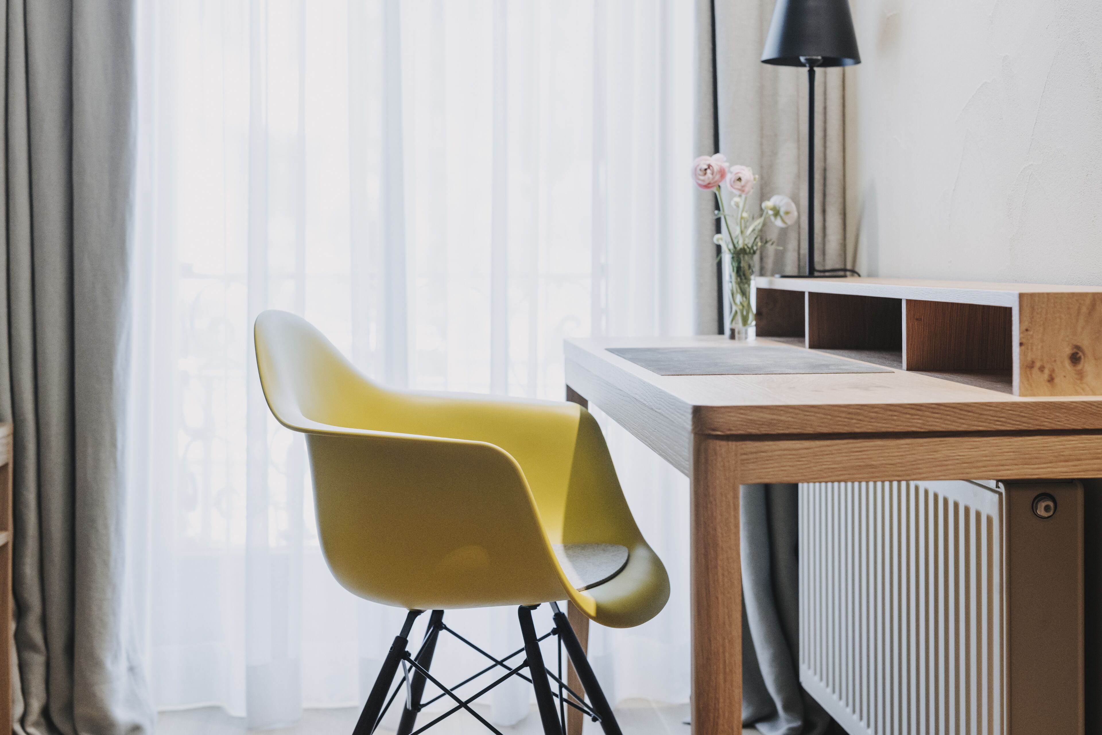Una habitación moderna con una silla amarilla, una mesa de madera, un radiador y una lámpara.