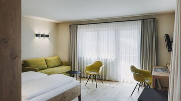 A hotel room with a bed, a green sofa, two yellow chairs, a small table, and a TV.