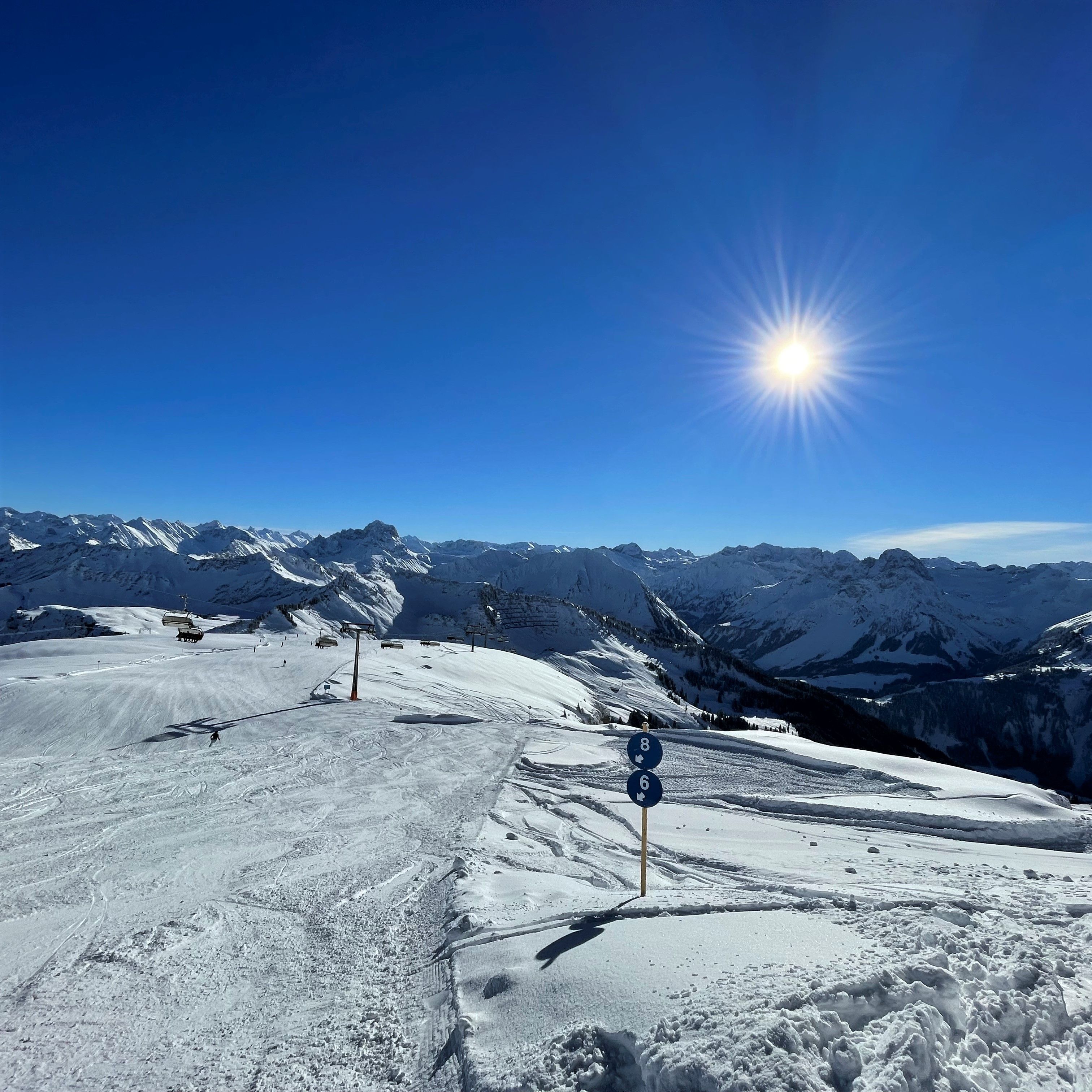 Une pente de montagne enneigée, avec des remontées mécaniques et un ciel dégagé.