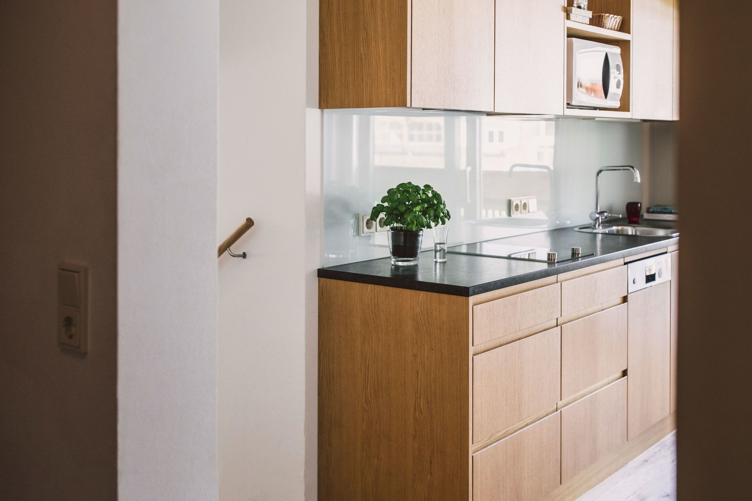 Eine moderne Küche mit Holzschränken, einer schwarzen Arbeitsplatte und einem Blumentopf.