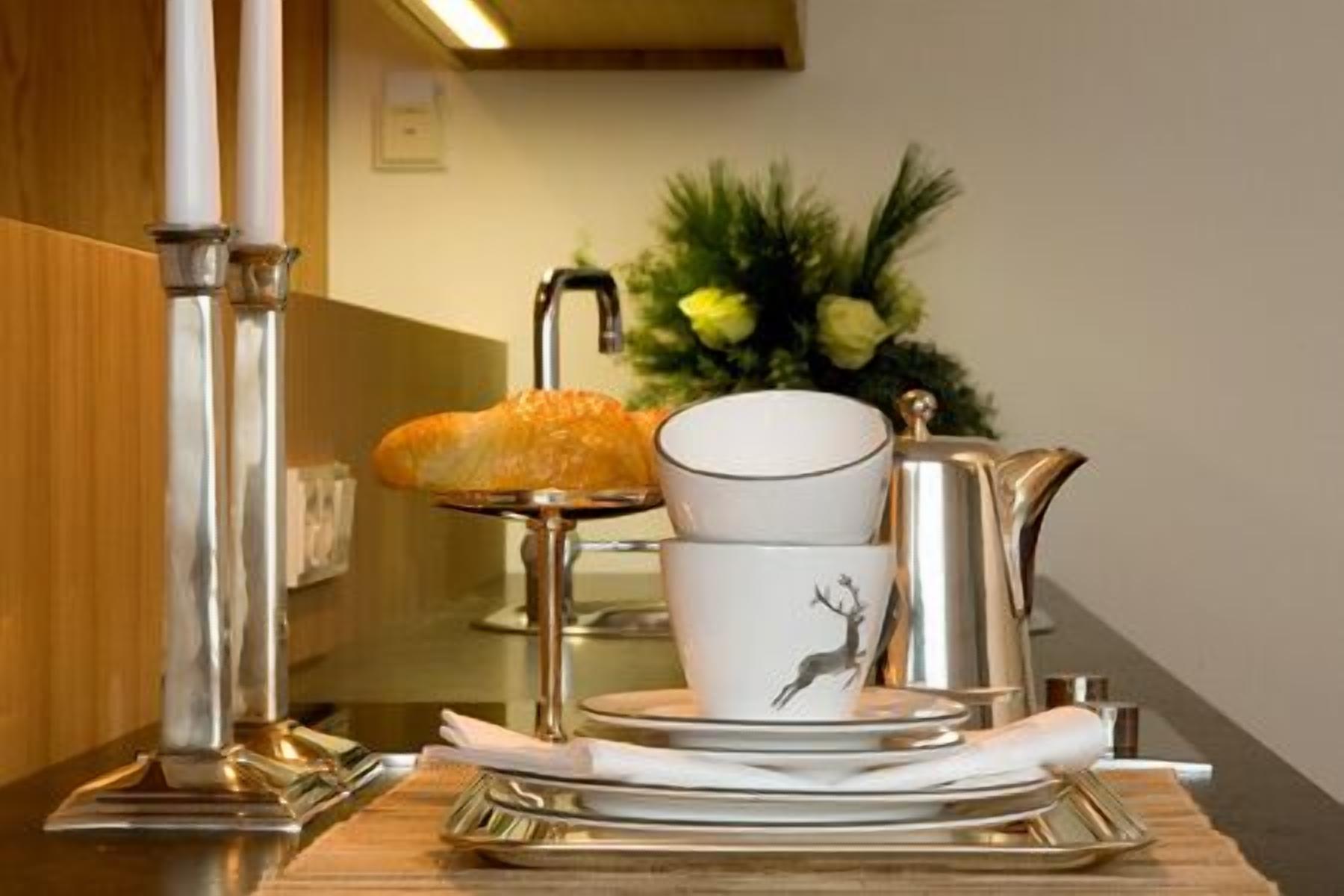 A breakfast setup with a plate of pastries, a coffee pot, a cup with a deer design, and a flower arrangement in the background.