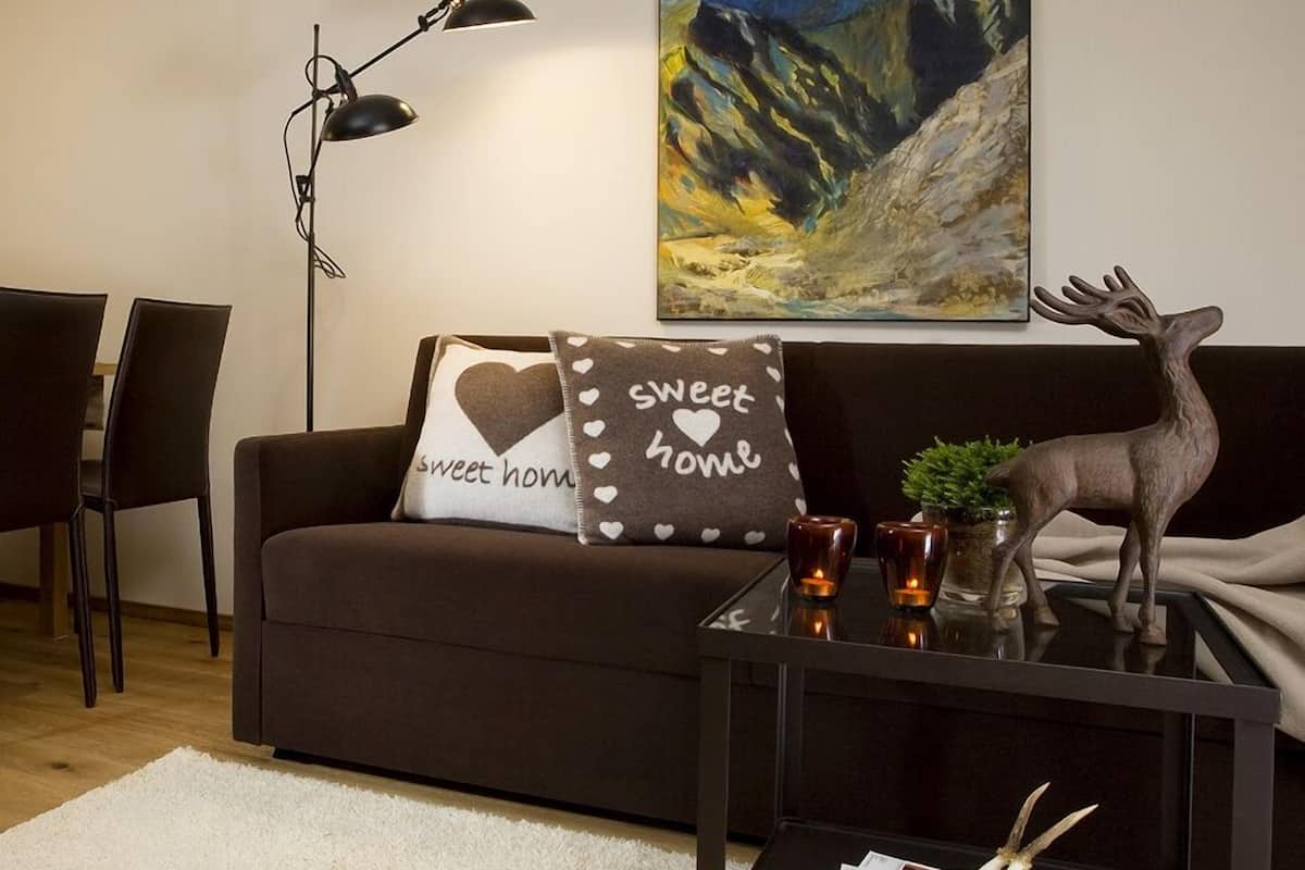 A modern living room with a brown sofa, a glass coffee table, a floor lamp, a painting of mountains, and a deer statue.