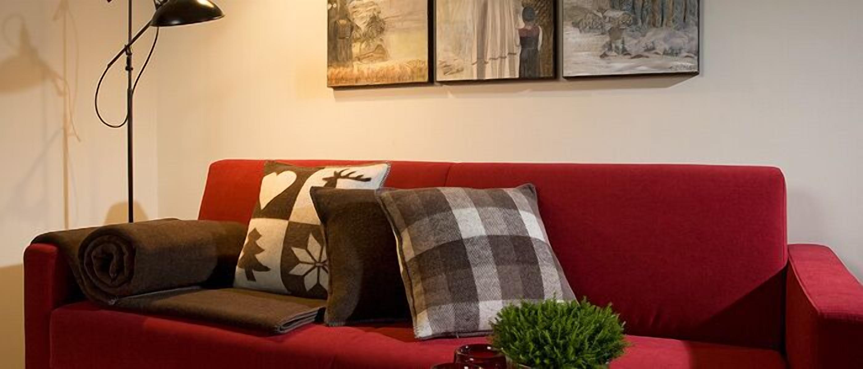 Un sofá rojo con cojines estampados, una pequeña planta y una lámpara de pie.