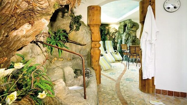 Un baño con piso de piedra, una columna de madera, zona de ducha y una planta.