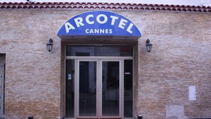 A brick building with a blue sign reading 'ARCOTEL CANNES' above a glass door entrance. - Arcotel (Cannes)