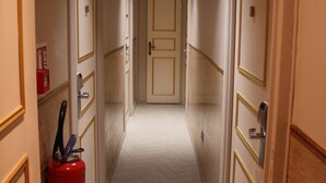 A narrow hotel hallway with doors on both sides, a fire extinguisher on the left, and a ceiling light. - Arcotel (Cannes)