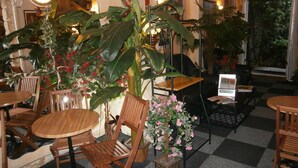 A restaurant with wooden tables and chairs, large potted plants, and a checkered floor. - Hôtel Beauséjour (Rouen)