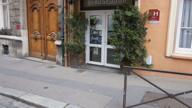 A hotel entrance with a wooden double door, a sign reading "HOTEL BEAUSEJOUR," and a small plant in front. - Hôtel Beauséjour (Rouen)