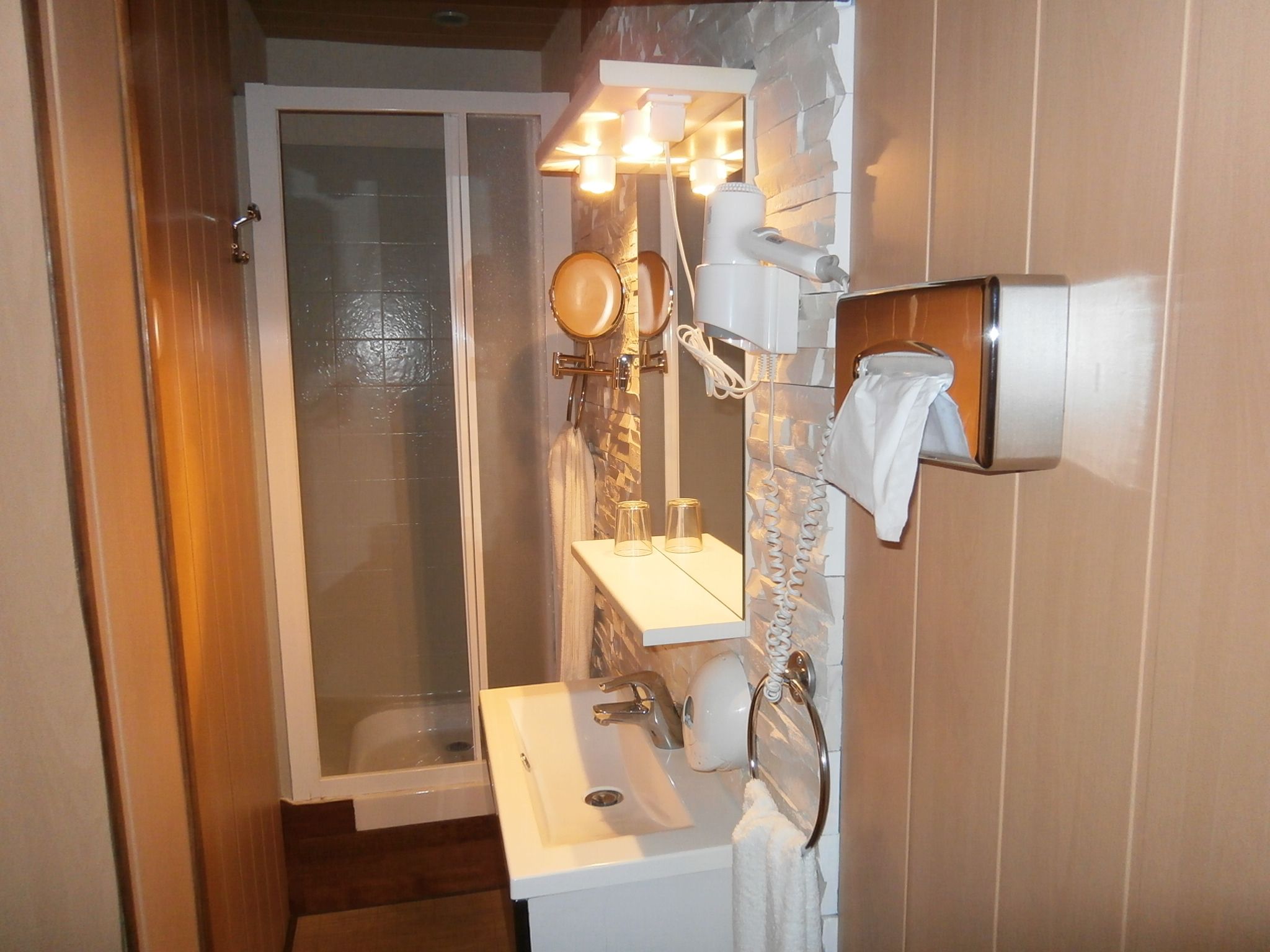 A bathroom with a glass shower door, a white sink, a mirror, and a towel rack.