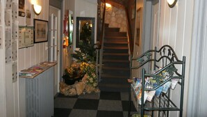 A hallway with a checkered floor, a staircase, and a magazine rack. - Hôtel Beauséjour (Rouen)