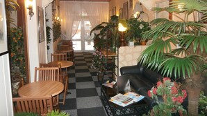 A cozy interior with a checkered floor, wooden furniture, and various plants. - Hôtel Beauséjour (Rouen)